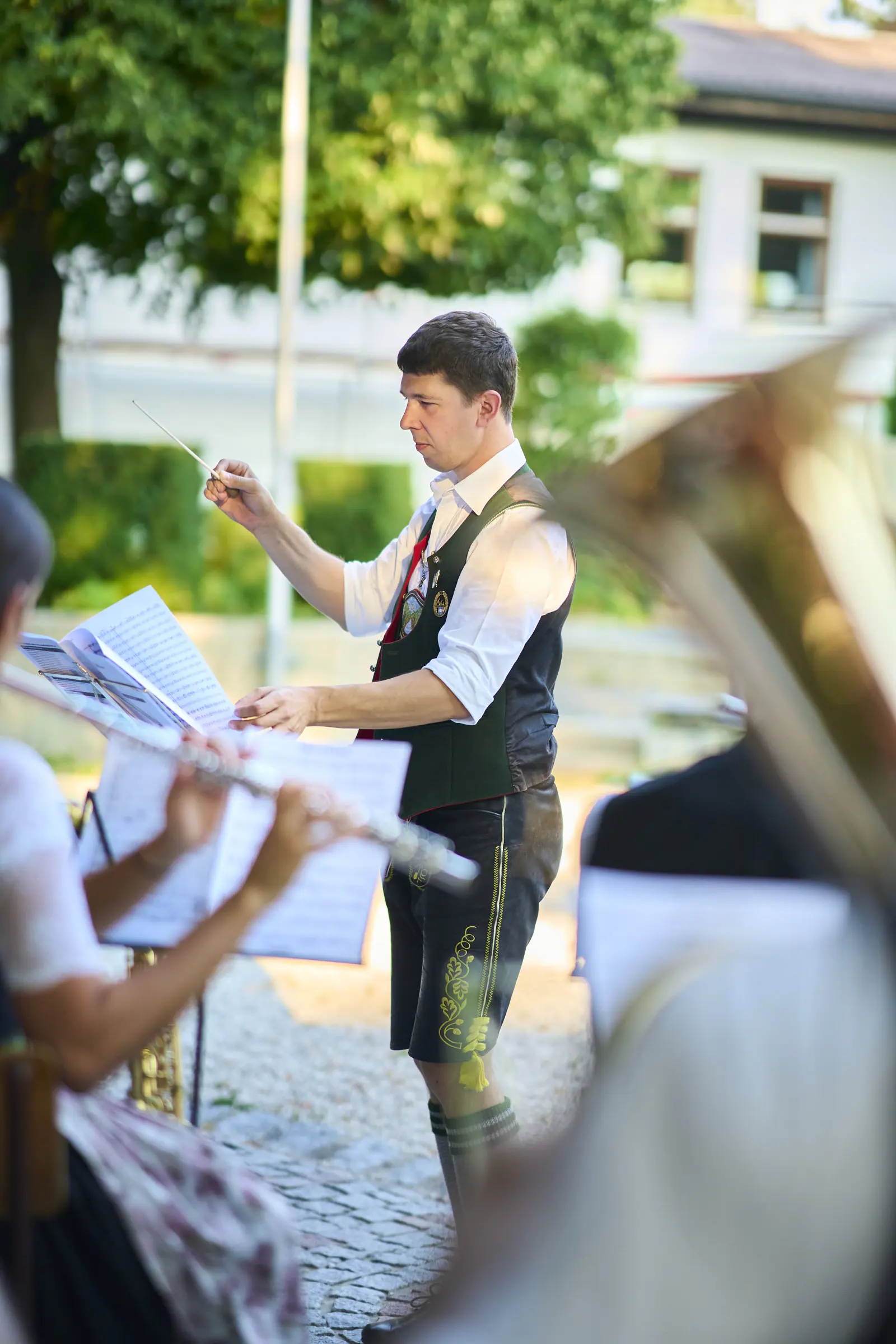 Mann dirigiert ein Blasorchester mit Flöte und Tuba, traditionelle Kleidung