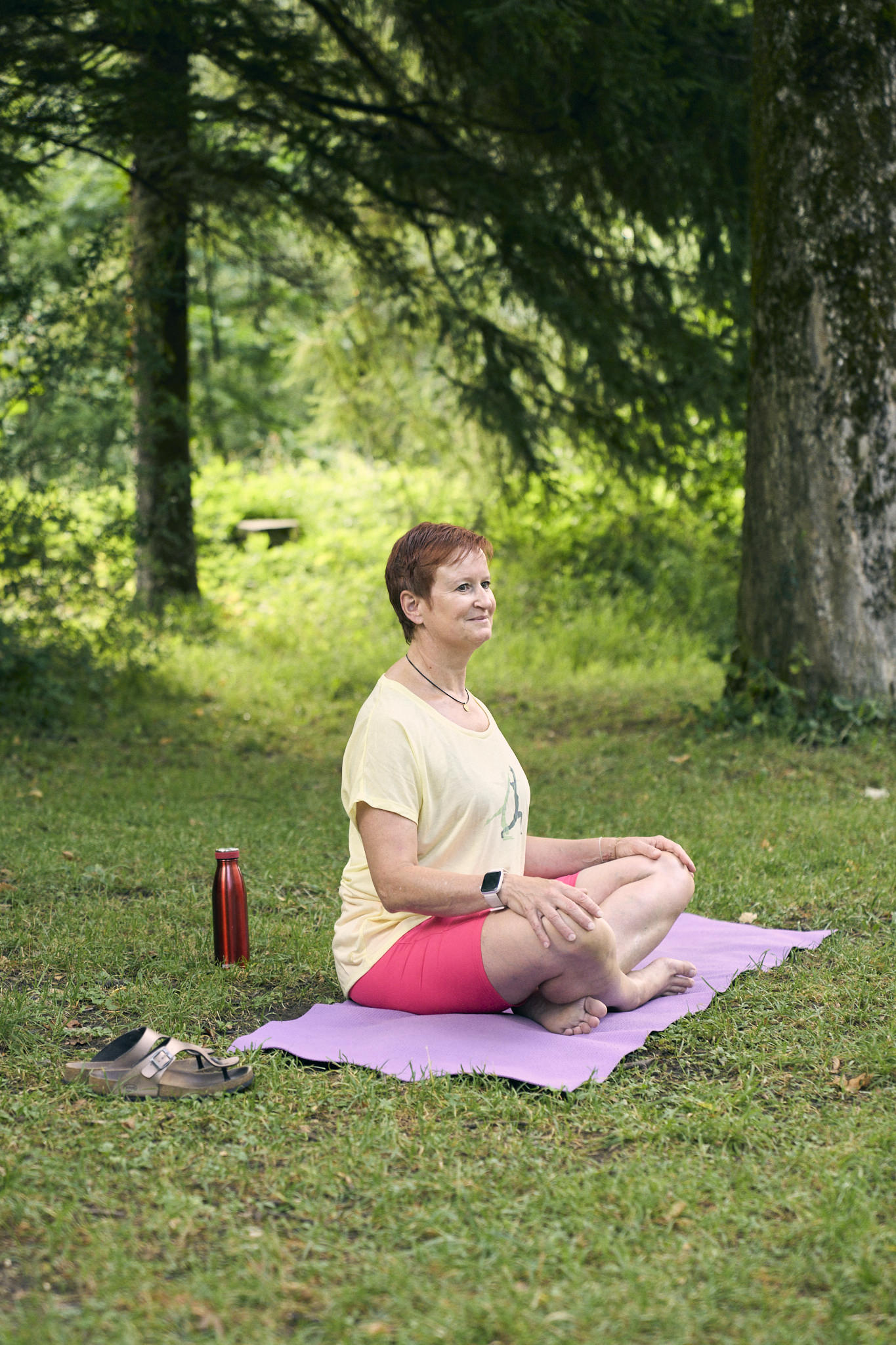 Ältere Frau meditiert auf einer Yogamatte im Freien.