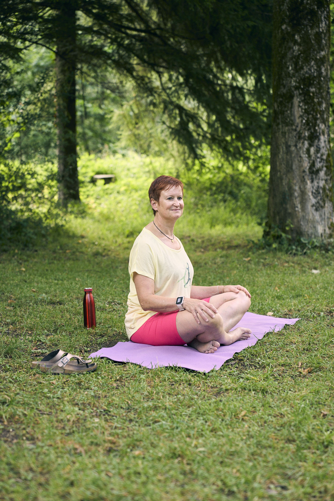 Frau in Yoga-Kleidung meditiert auf einer Matte im Wald.