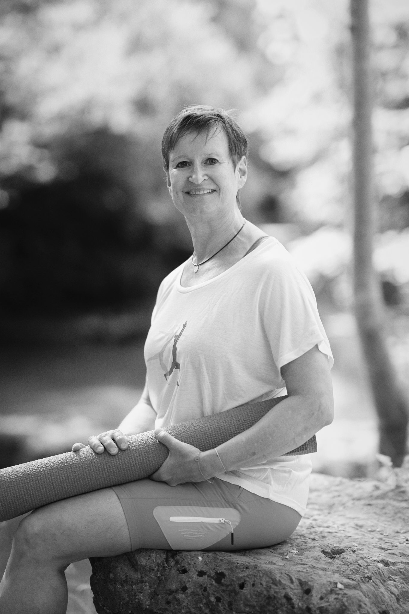 Frau mit Yogamatte lächelt in der Natur.