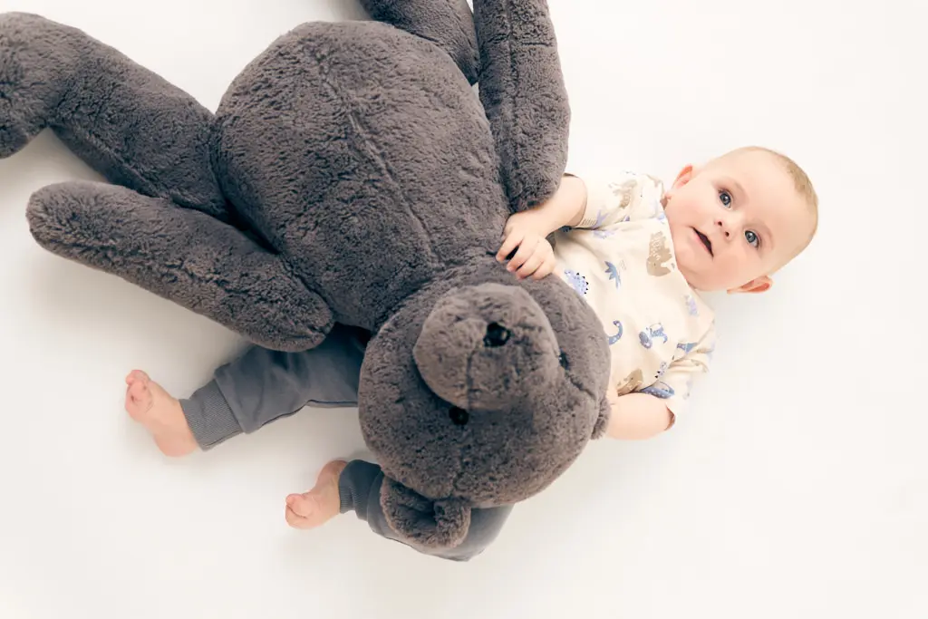 Baby spielt mit großem Teddybär auf weißem Hintergrund.